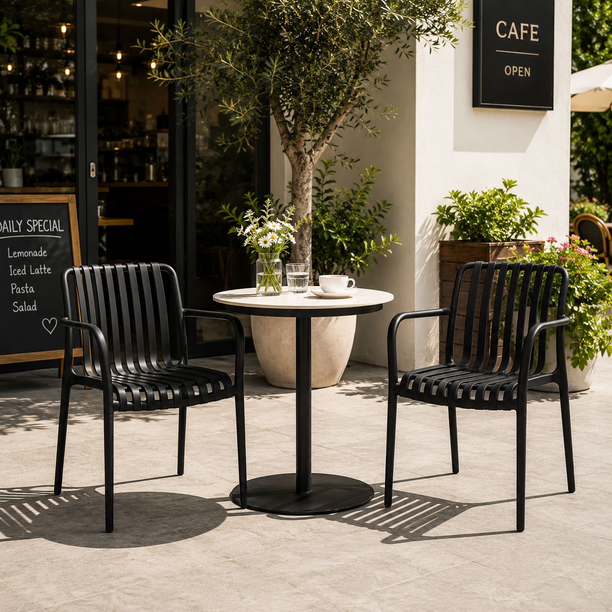 Matte black slat-back stackable polypropylene armchairs with integrated armrests in an outdoor café patio with a round bistro table and high-contrast natural daylight.