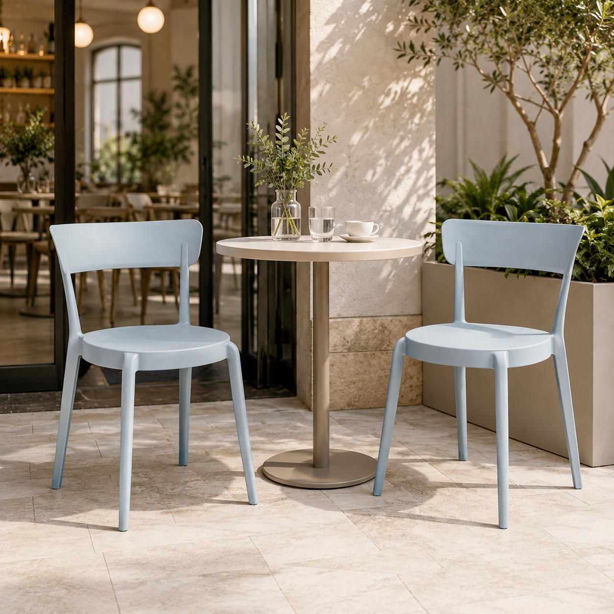 Stackable polypropylene café side chairs in soft blue arranged on outdoor terrace with round bistro table, stone paving and garden courtyard backdrop — PC-72.