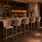 Channel-stitched velvet counter stools at restaurant counter dining in Mushroom Taupe, marble worktop with open kitchen backdrop and warm ambient lighting, BC-90