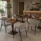 Wraparound open-back dining armchairs in pebble grey mélange woven fabric, paired with walnut pedestal tables in a boutique café interior, DC-1536