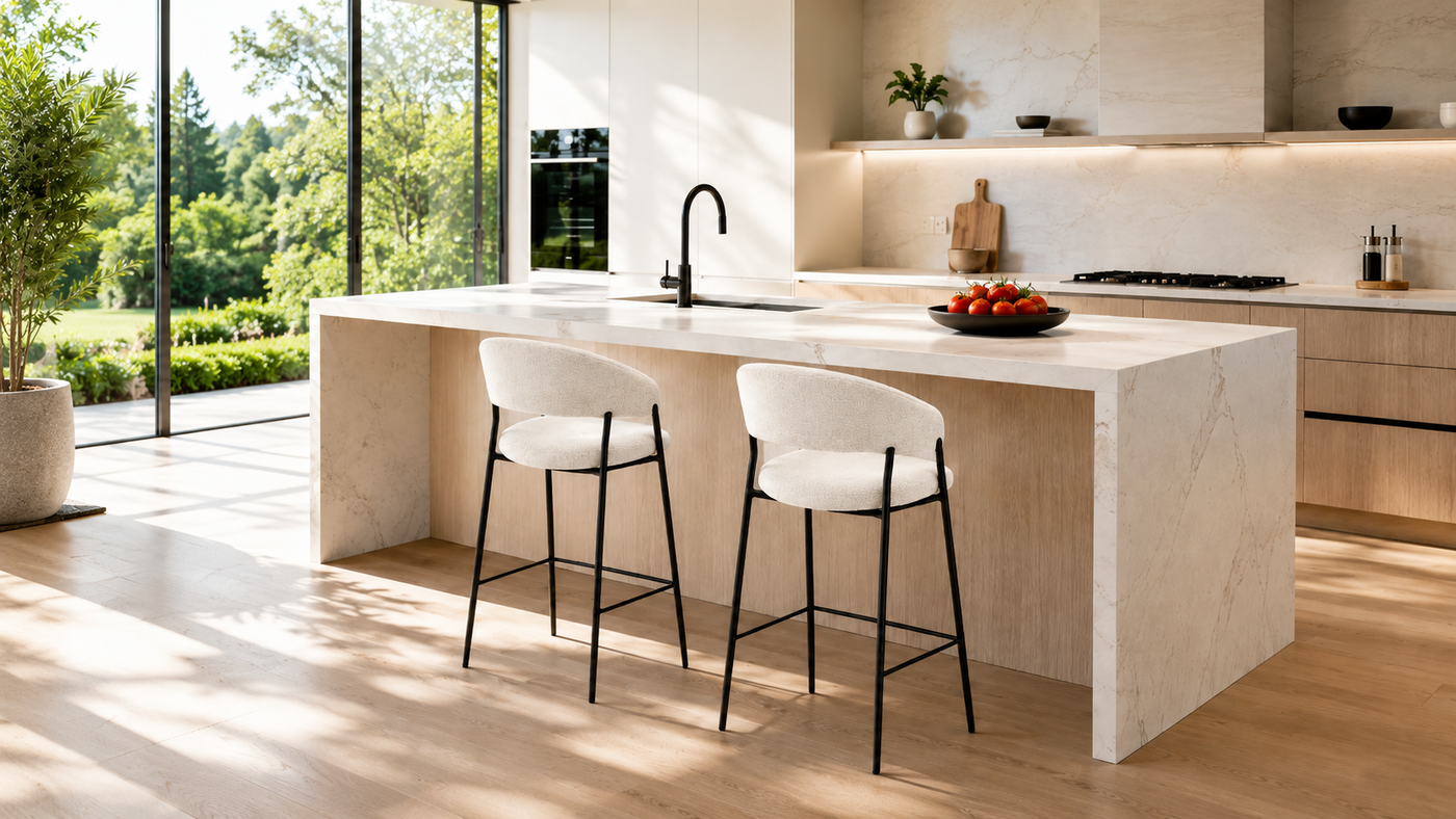 Low-back wraparound upholstered counter stools in ivory textured fabric at a modern kitchen island with slim matte black metal frames and natural daylight.