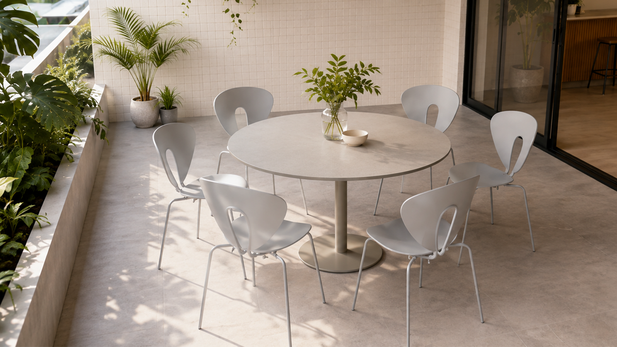 Six pebble grey cut-out back polypropylene side chairs arranged around a round table on a modern indoor terrace with tropical plants, PC-96