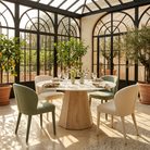 Round sintered stone dining table in a sunlit arched glass conservatory with upholstered chairs, T-132