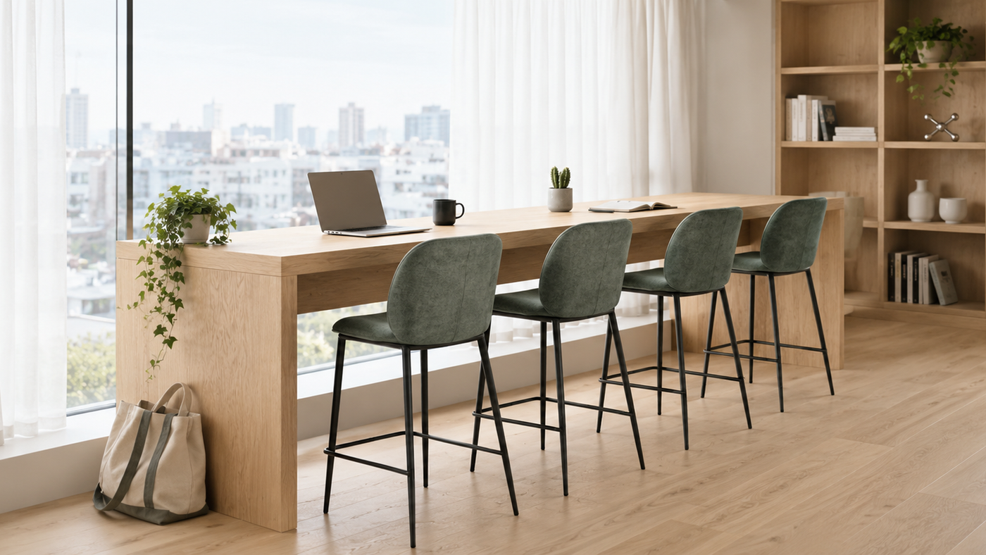 Sage green linen-look rounded-back counter stools along timber work counter in bright shelf-lined studio interior with city views, BC-75