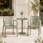 Soft sage green slat-back stackable polypropylene armchairs with integrated armrests in an outdoor café patio with a round bistro table and high-contrast natural daylight.