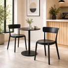 Stackable polypropylene café side chairs in matte black paired with round bistro table in open-plan residential kitchen dining area with timber cabinetry and large windows — PC-72.
