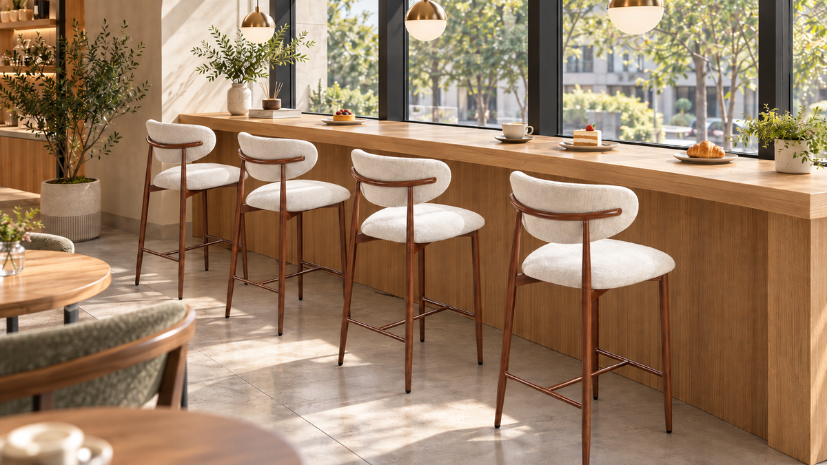 Upholstered bar stools in ivory white along a window-side café counter, showing rounded backs and open steel rails, BC-157-750