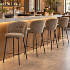Upholstered bar stools arranged in a row along a hospitality-style bar counter, showing repeated rounded back profiles, BC-153-750